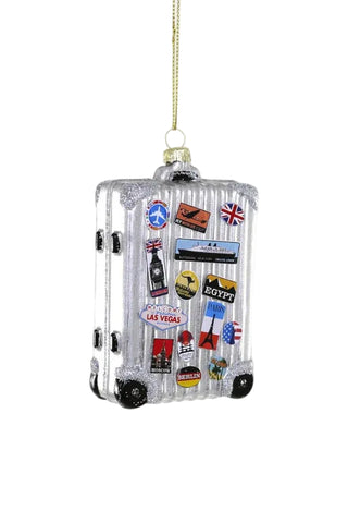 A silver ribbed suitcase-shaped hanging ornament decorated with colorful travel stickers, shown against a plain light gray background.