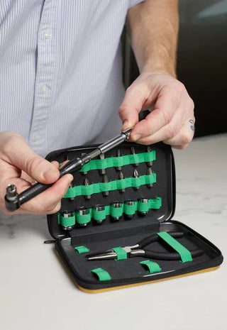 Person using a screwdriver from a black and green tool set on a light surface.